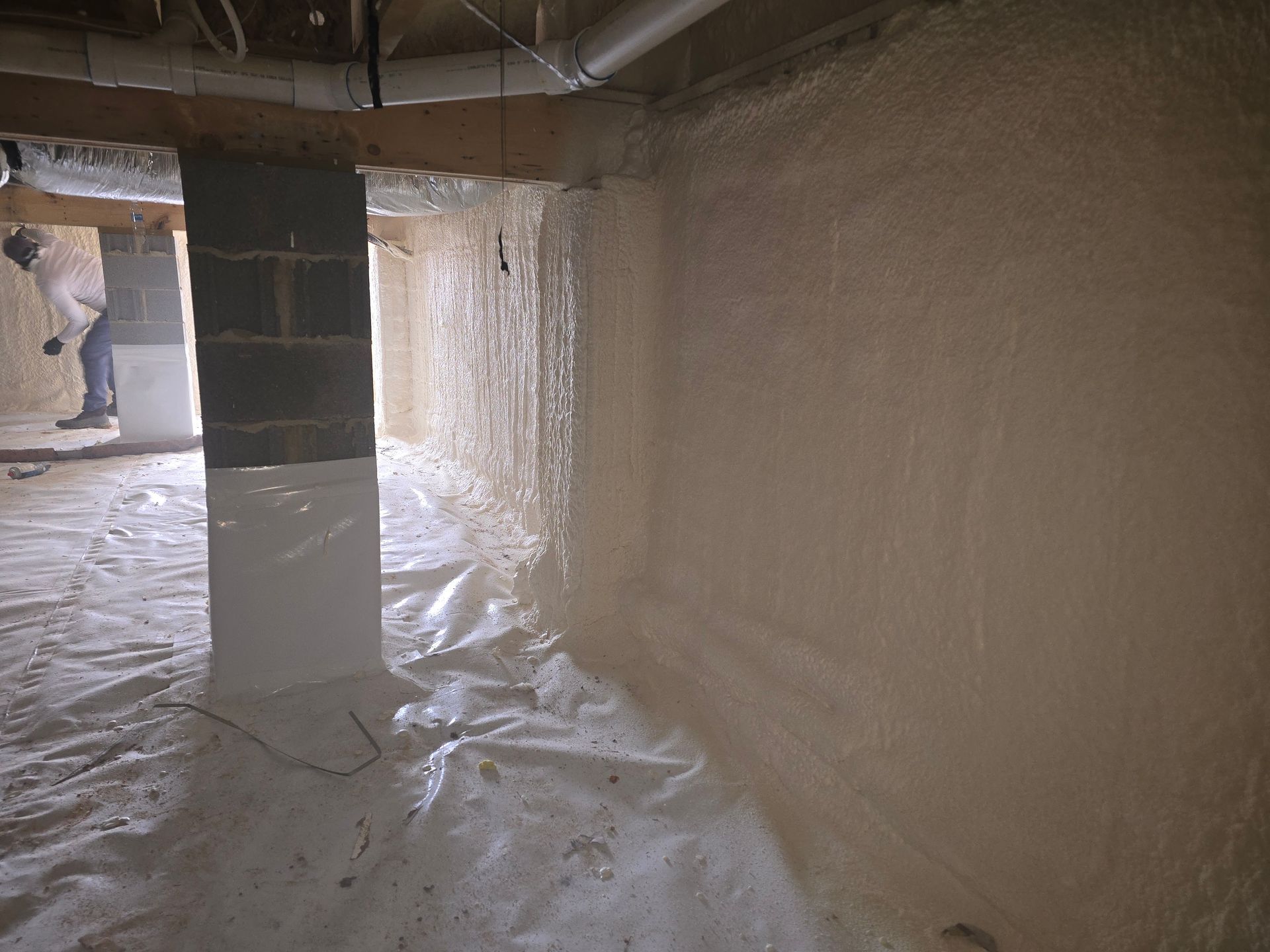 Basement interior with spray foam insulation being applied to walls.