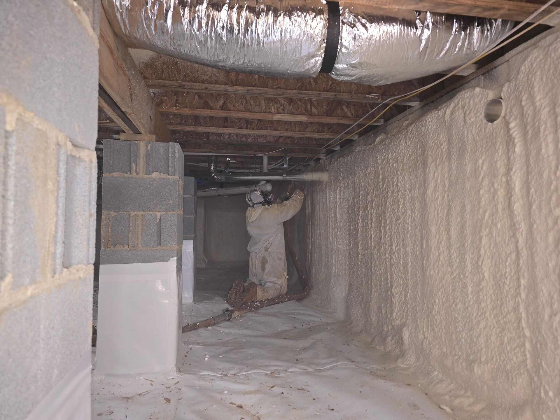 Worker sprays foam insulation on crawl space walls.