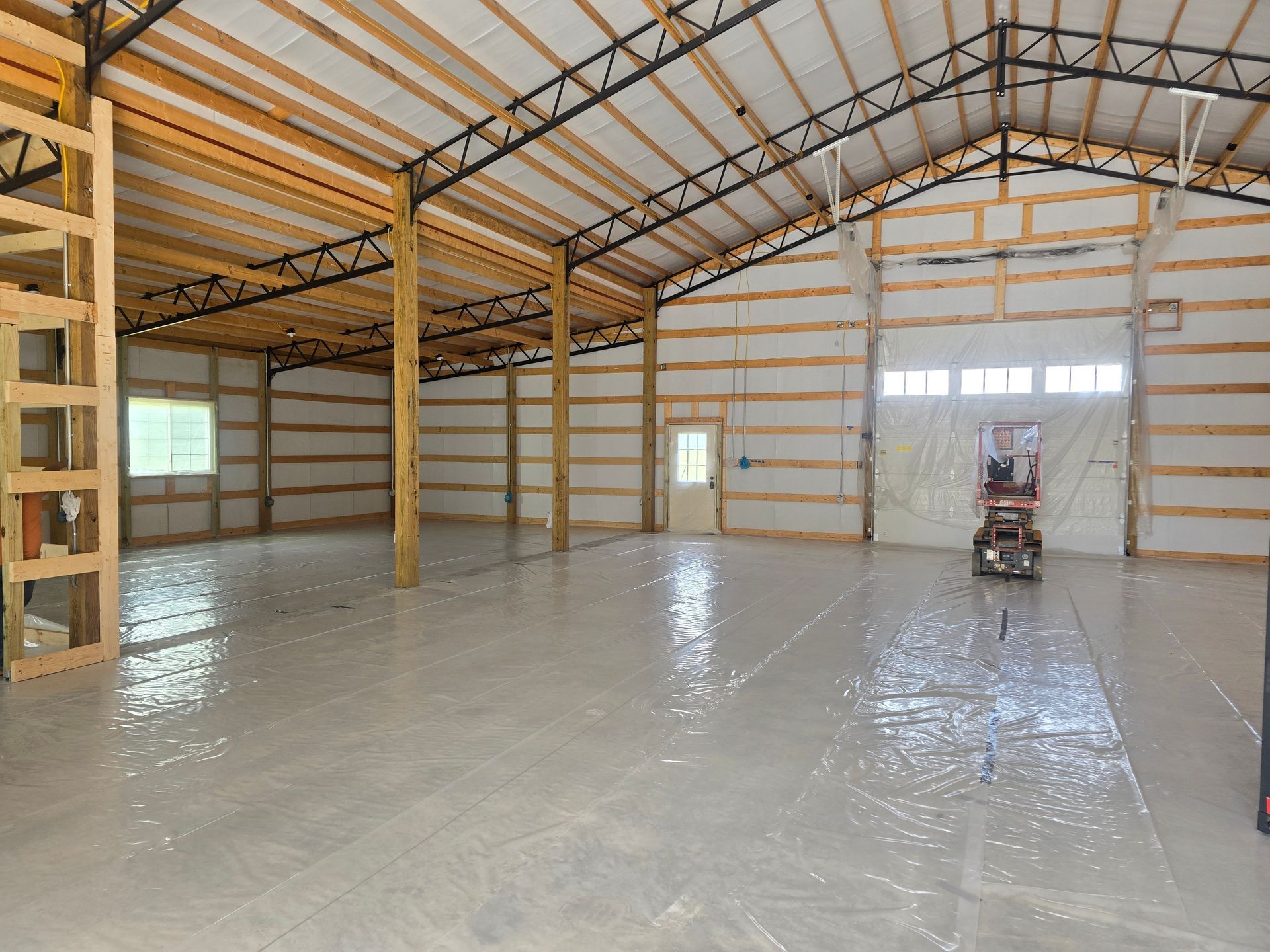 Interior of a large, empty metal building with a concrete floor and exposed wooden framing.
