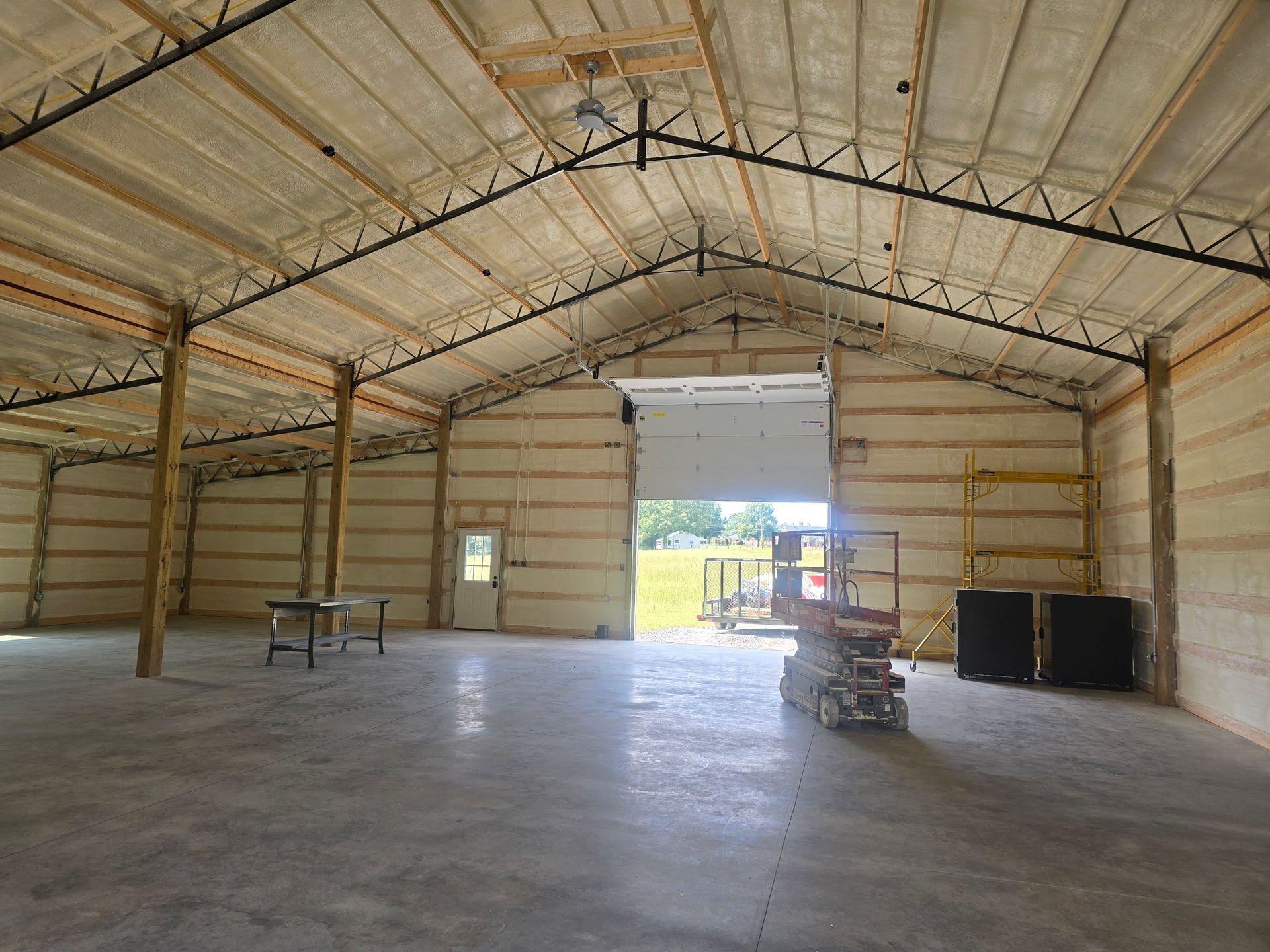 Interior of a large warehouse with foam insulation, open door, and concrete floor.