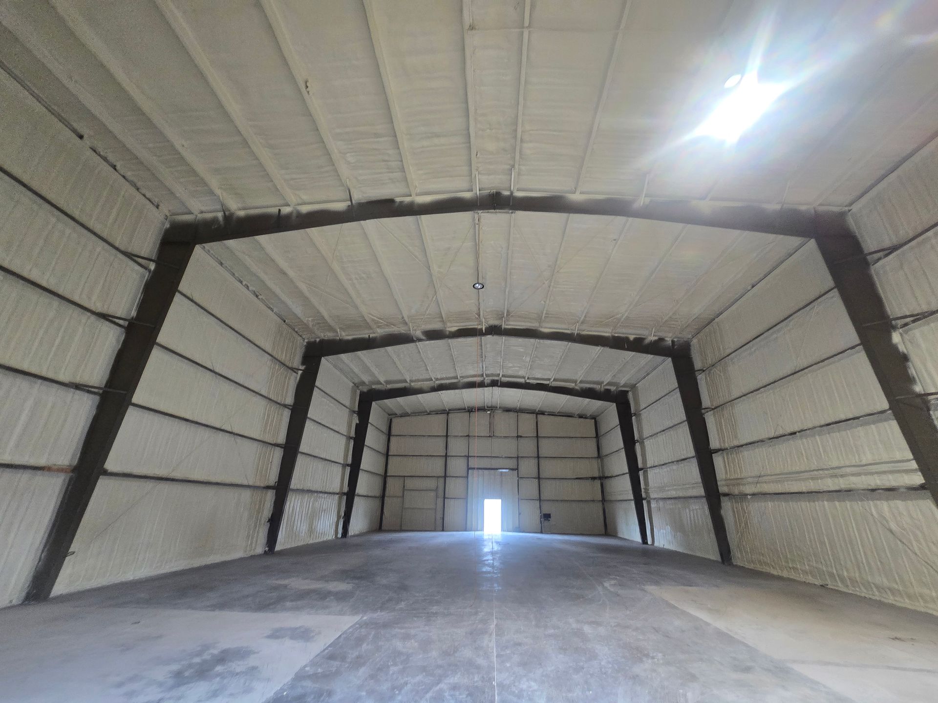 Interior view of a large industrial building with white foam insulation on the walls and ceiling, concrete floor.