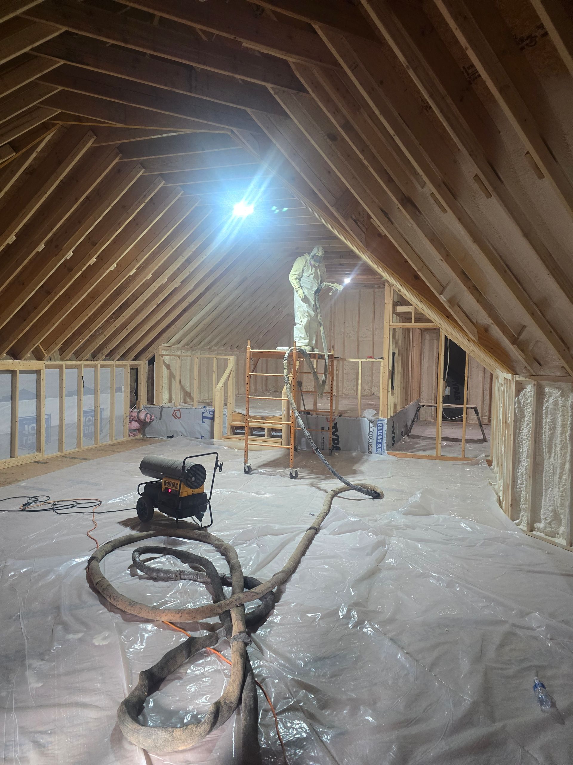 Interior of an attic under construction, with wooden beams, insulation, and equipment.