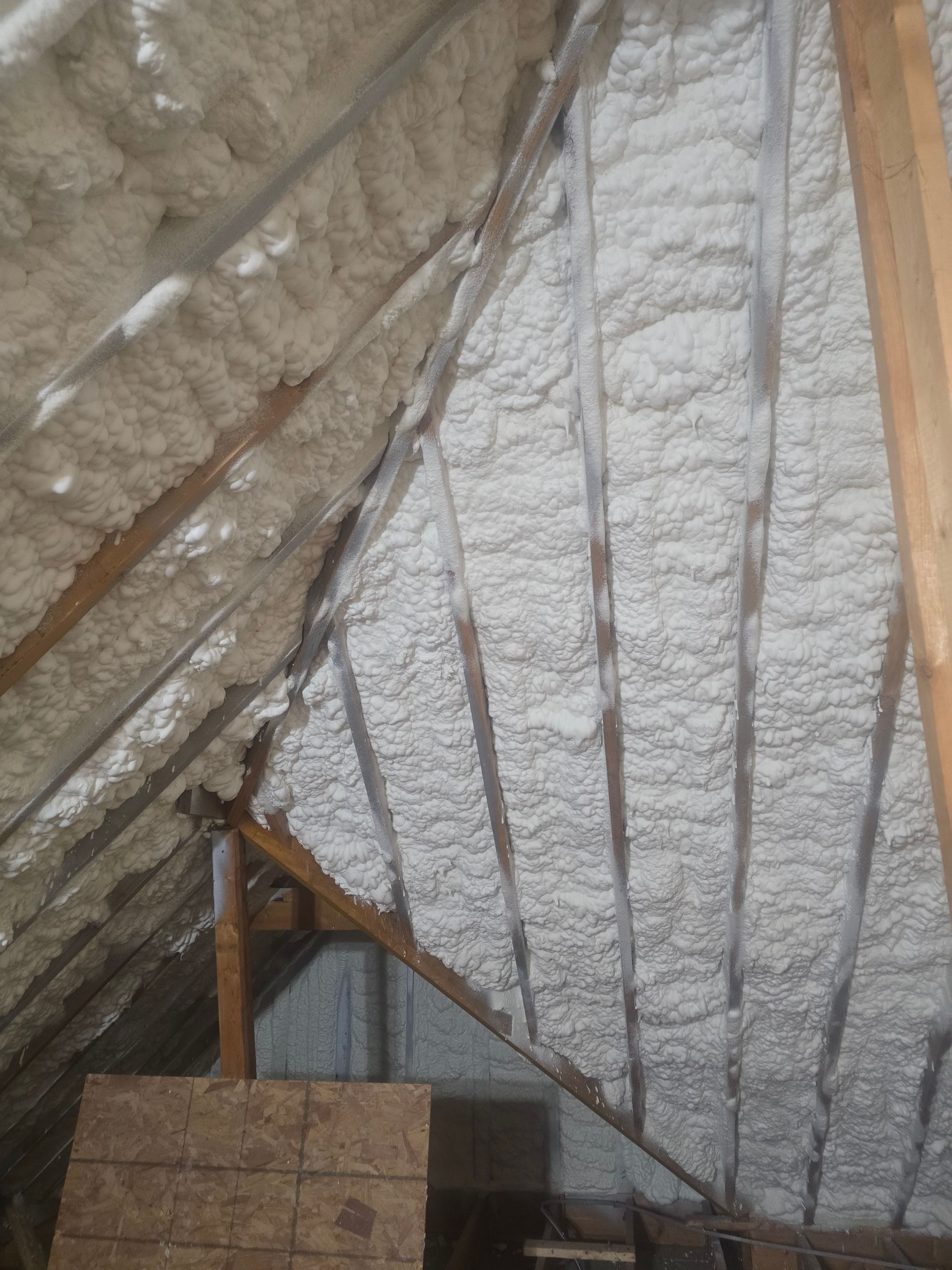 Attic with white spray foam insulation between wooden rafters.