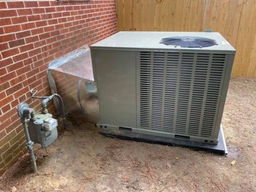 A large air conditioner is sitting on the ground next to a brick wall.