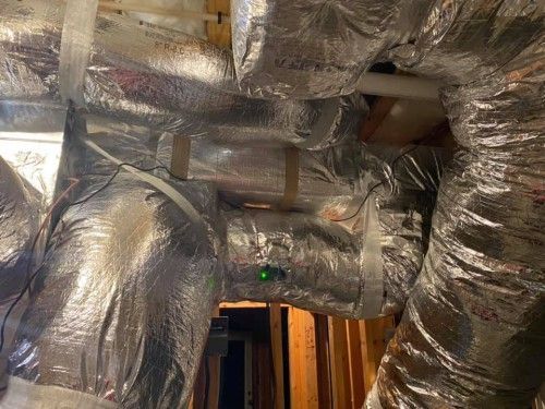 A bunch of ducts wrapped in foil are hanging from the ceiling.