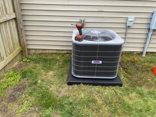 An air conditioner is sitting in the grass next to a house.