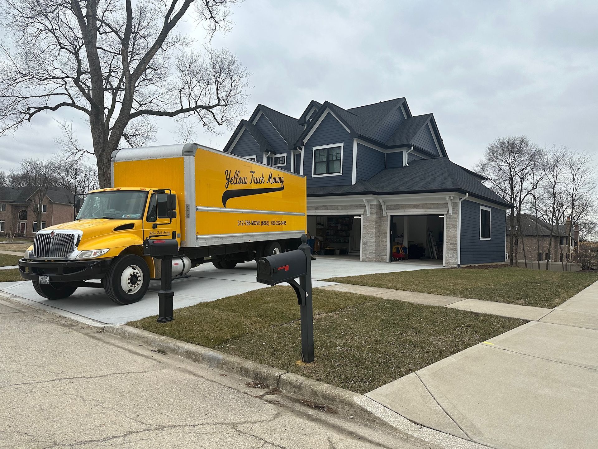 Yellow moving truck parked in front of a blue house with open garage doors.