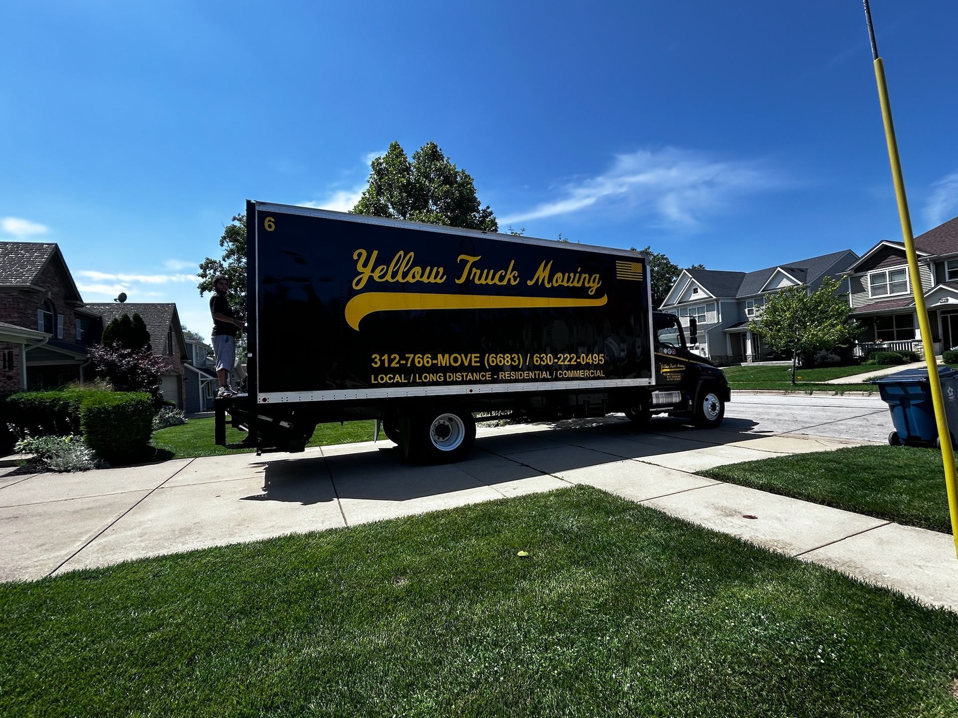 Yellow Truck Moving truck parked on a residential driveway on a sunny day.