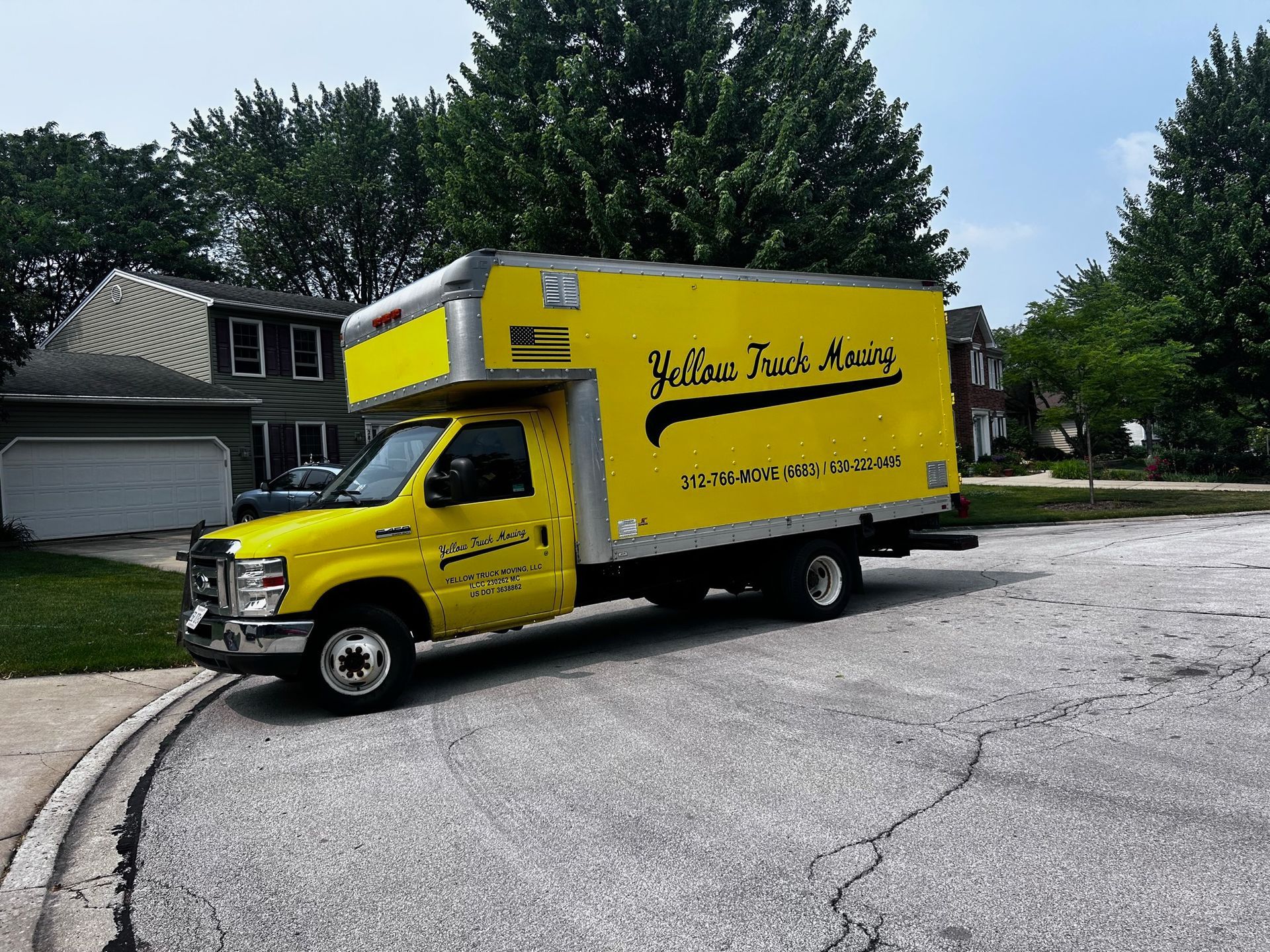 Yellow box truck parked on a residential street. Truck has business name 