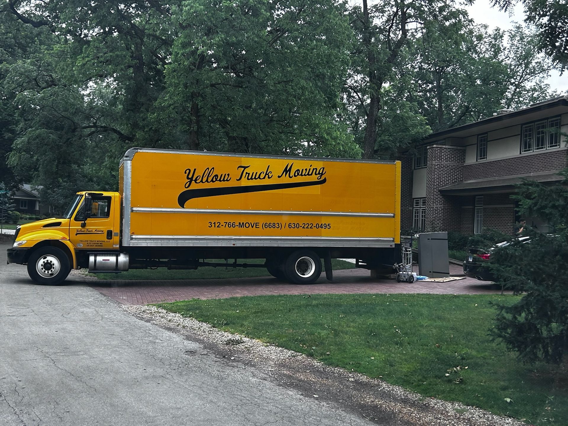 Yellow moving truck parked in front of a house. The truck has 