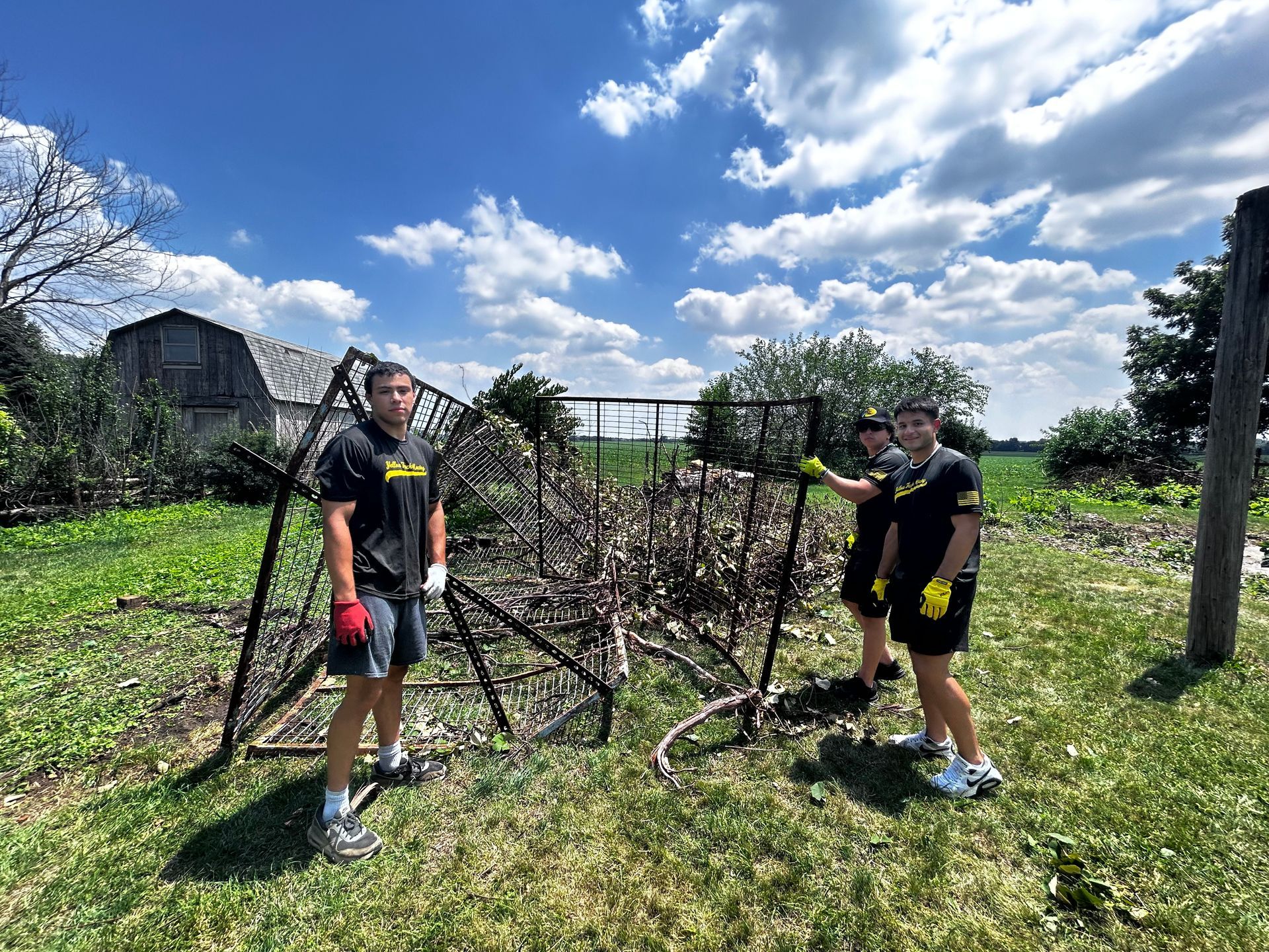 Three people clearing debris from a metal structure outdoors under a blue sky.