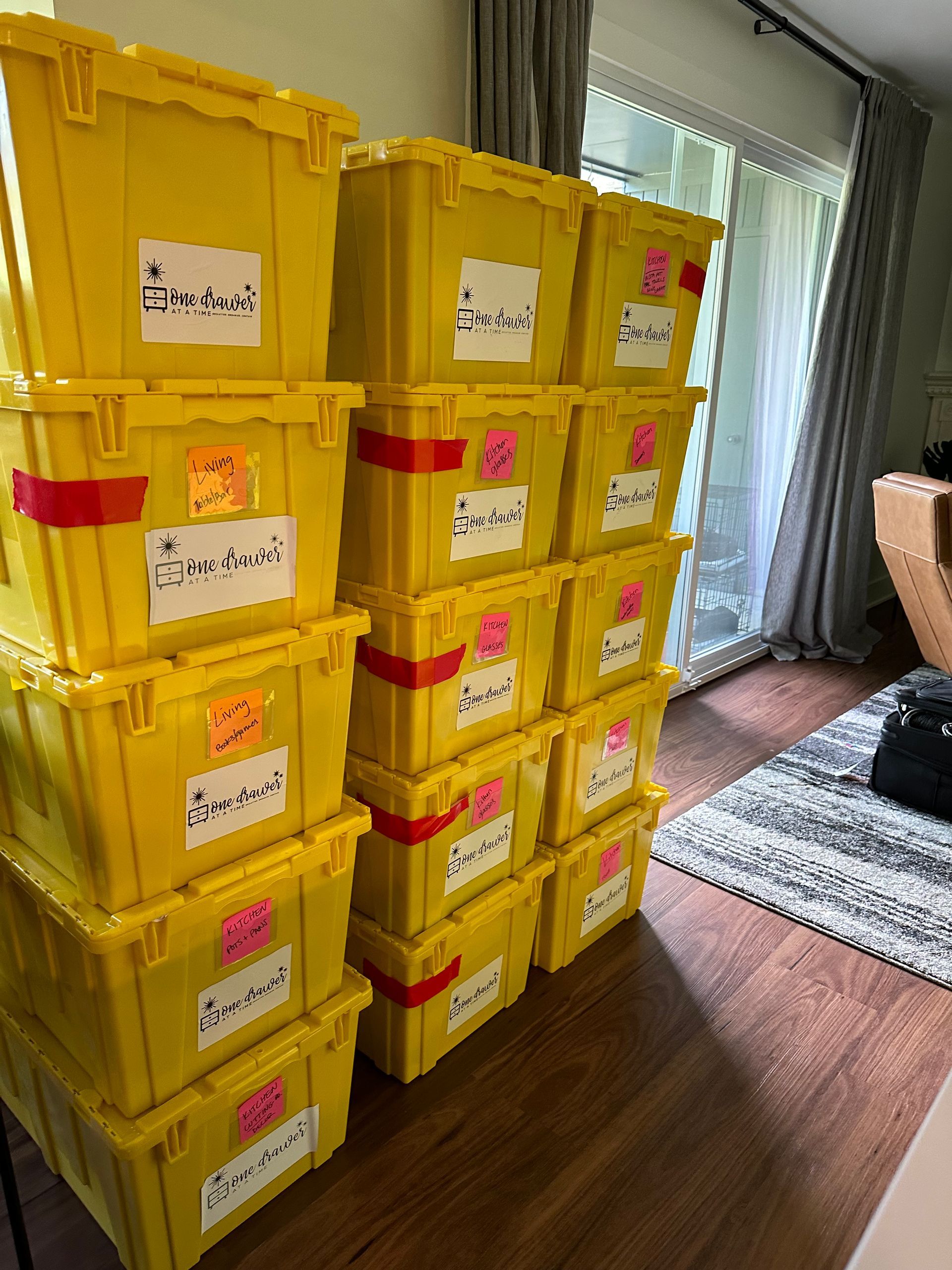 Yellow storage bins stacked with labels on a wooden floor near a sliding glass door.