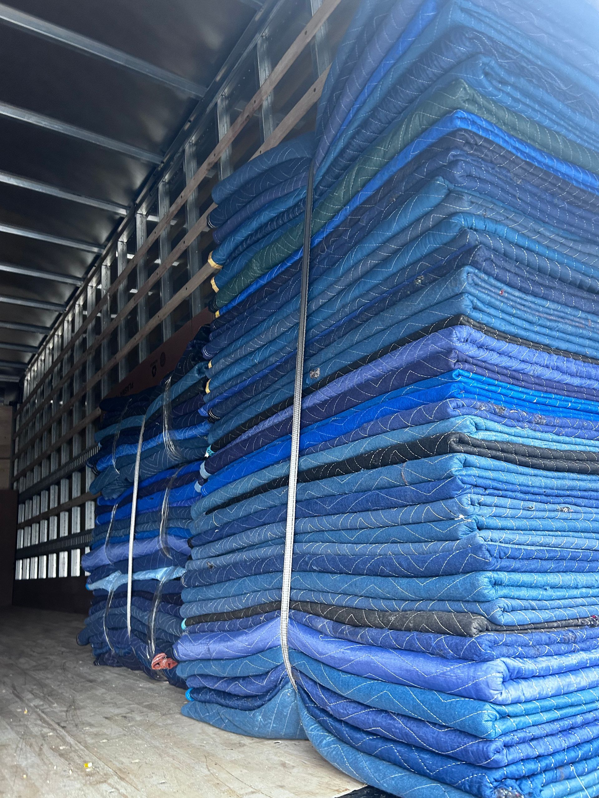 Stacks of blue moving blankets inside a truck, secured with white straps.