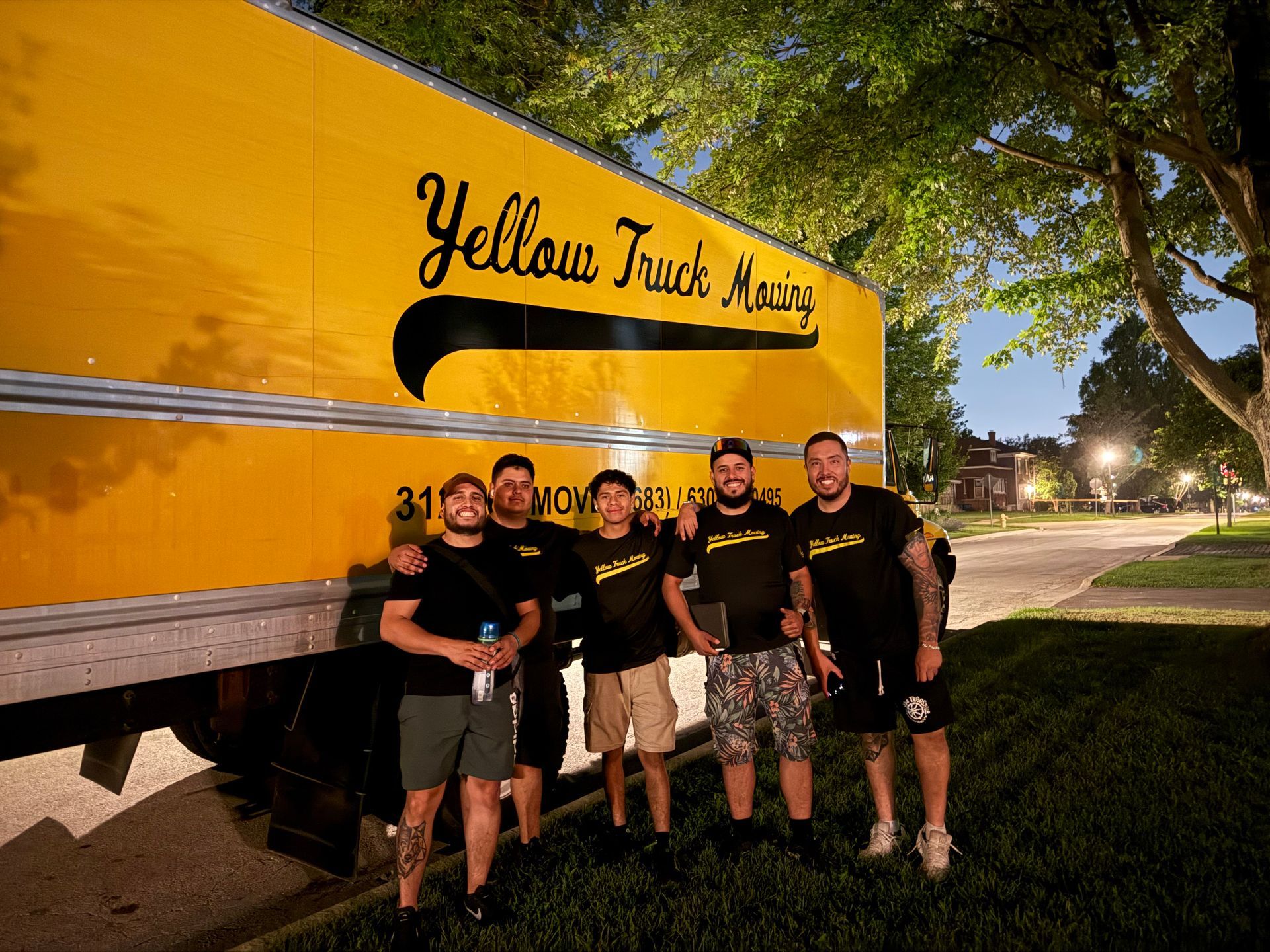 Five men pose by a large yellow moving truck, 