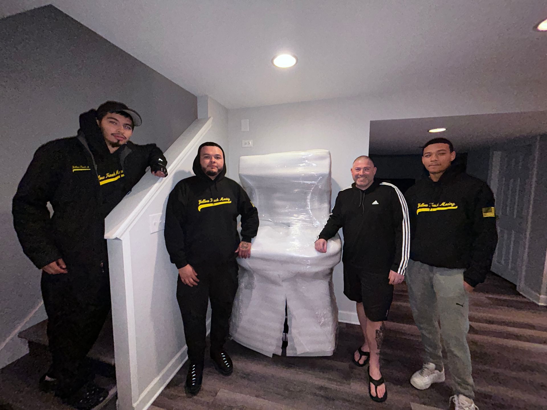 Four movers with a wrapped object in a hallway, posing.