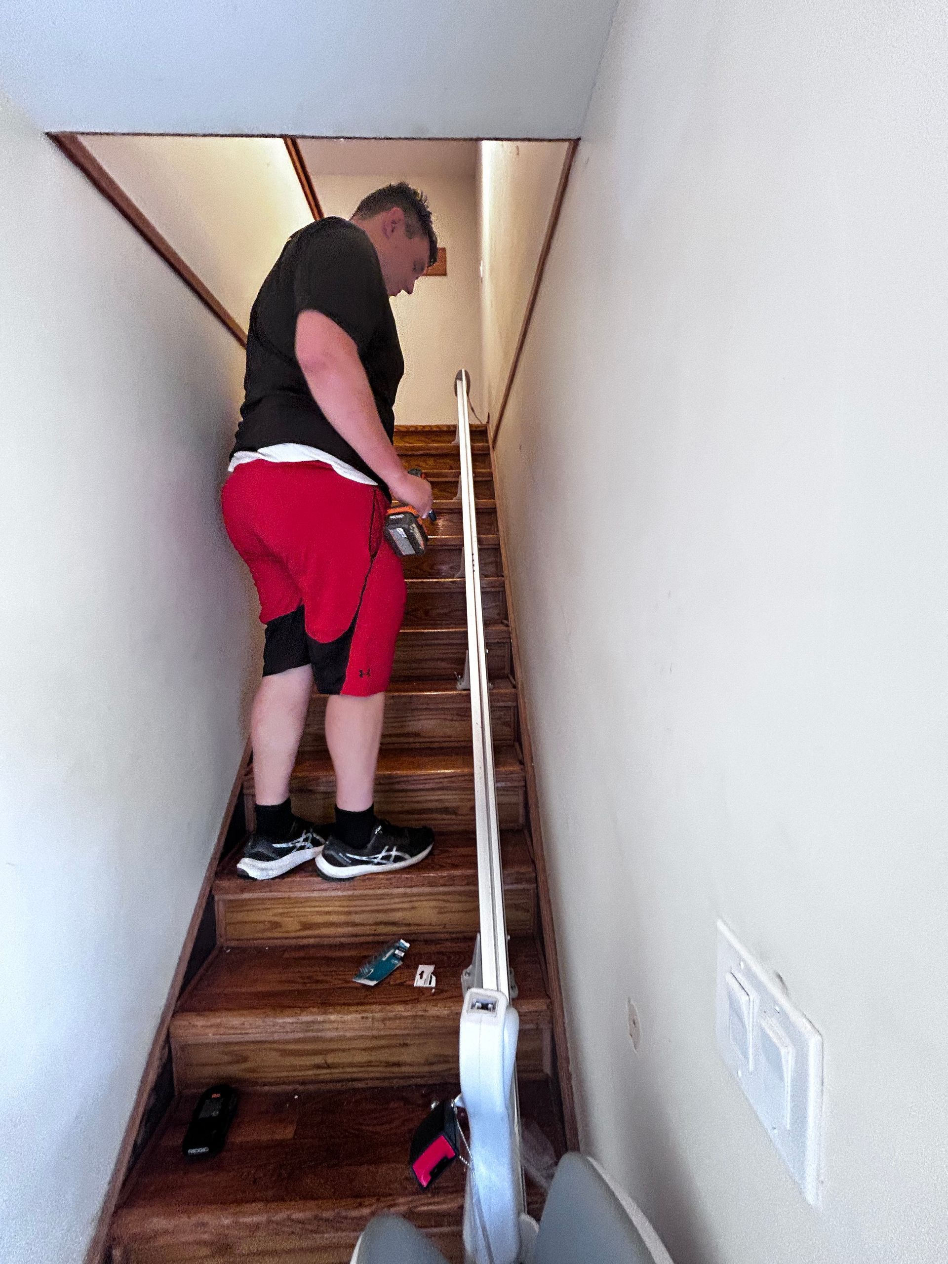 Person in red shorts on a wooden staircase with a handrail, possibly repairing something.