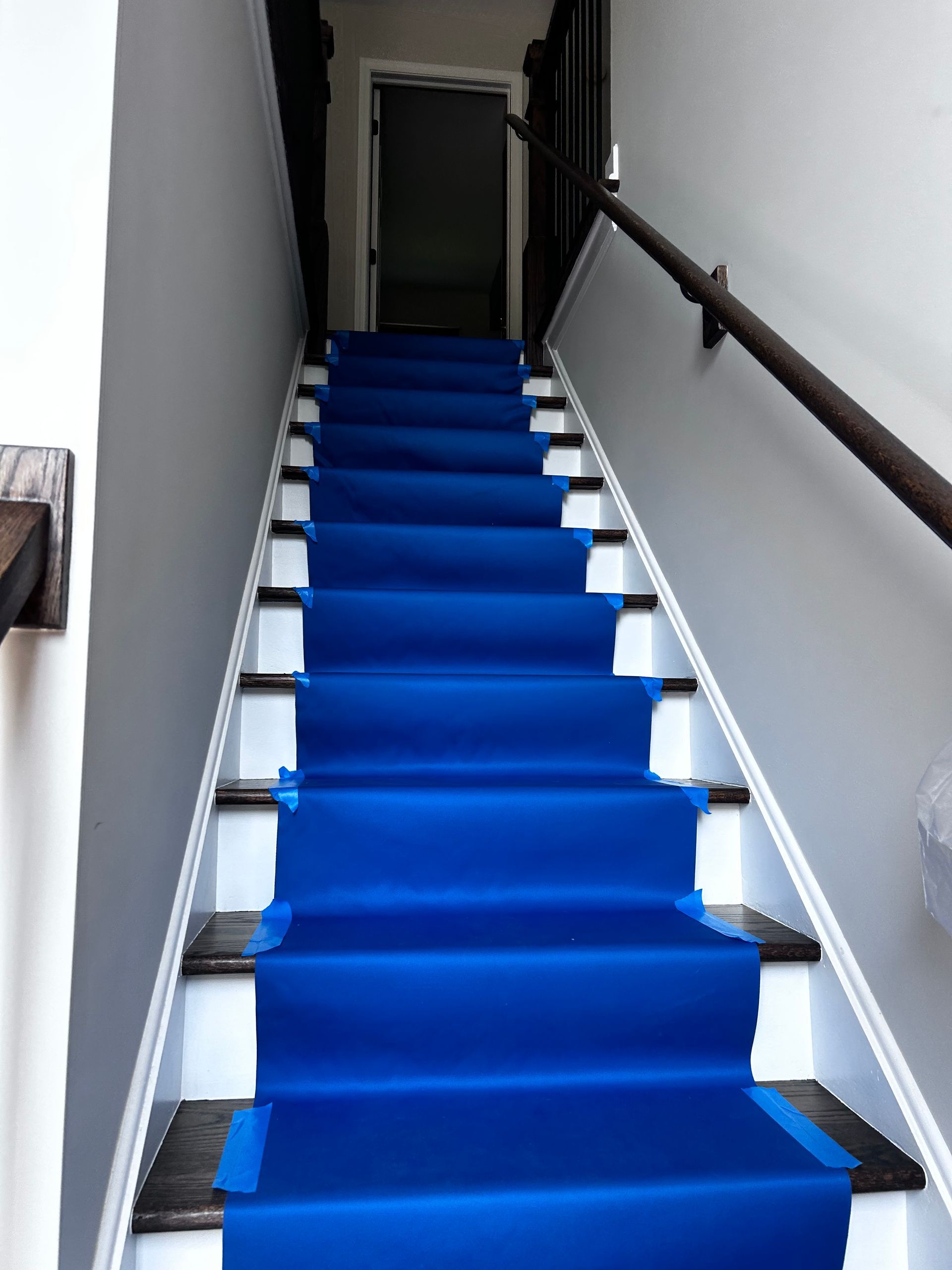 Blue carpet runner on wooden stairs with white risers and gray walls.
