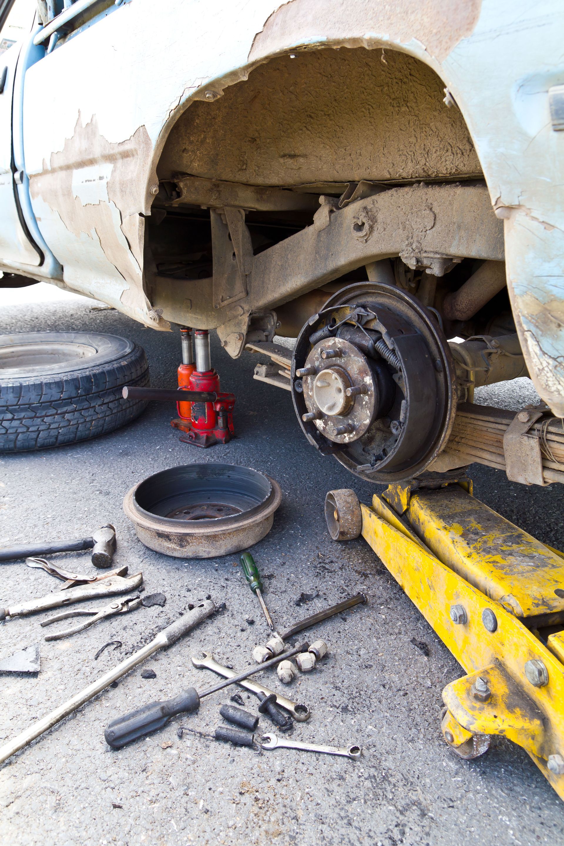 A tire well without a tire surrounded by tools while on a yellow jack.