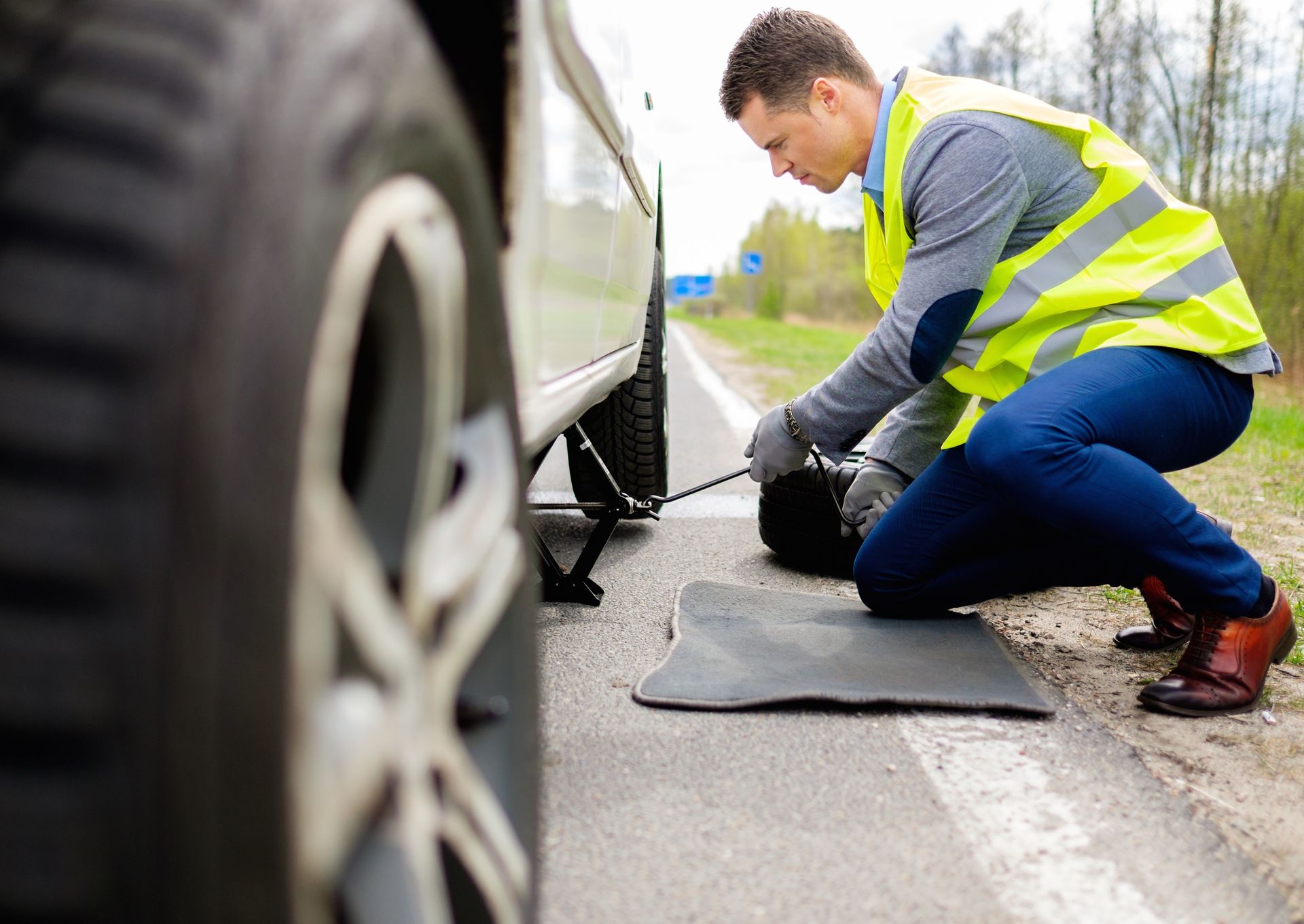 A man wearing a safety vest is changing a tire.