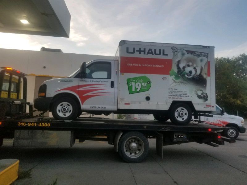 A u-haul truck is sitting on top of a tow truck.