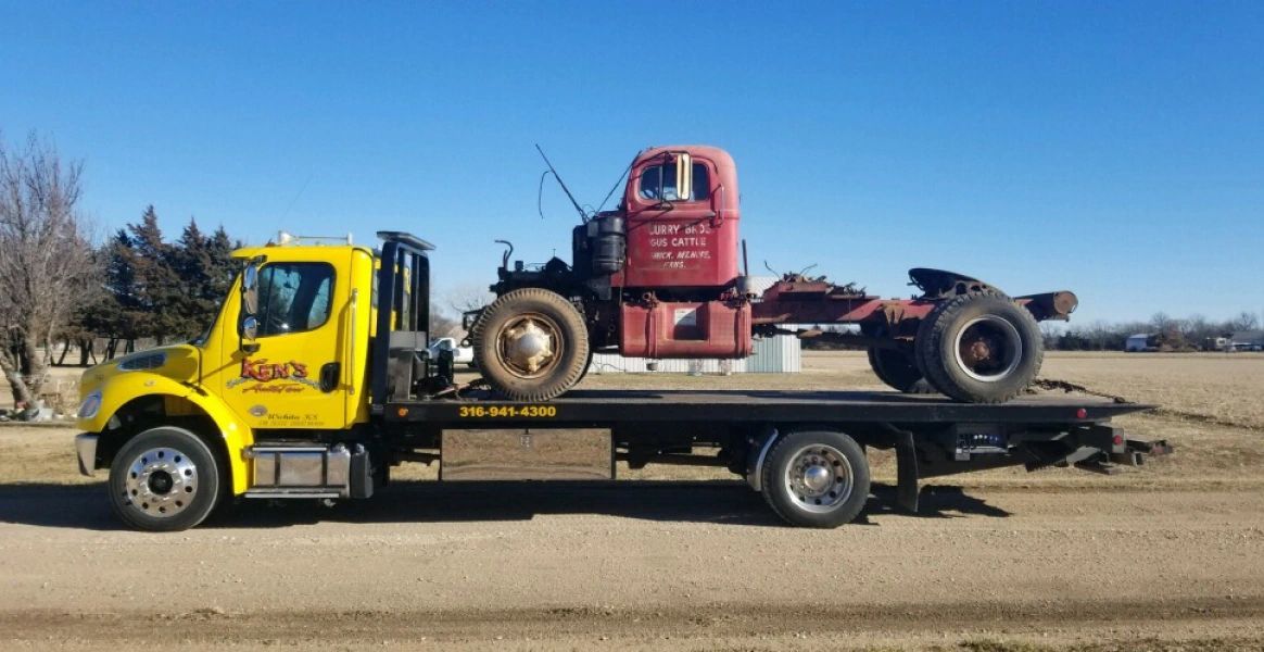 A yellow tow truck is carrying a red truck on its flatbed.