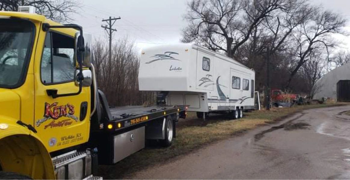 A yellow tow truck is towing a rv down a road.