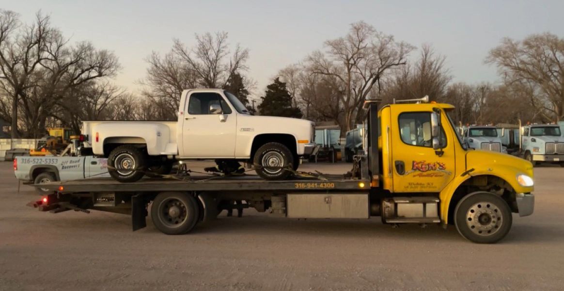 A yellow tow truck is towing a white truck.