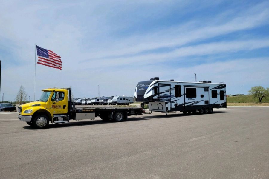 A yellow tow truck is towing a rv in a parking lot.