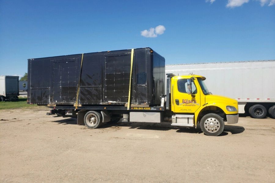 A yellow tow truck is carrying a large black box.