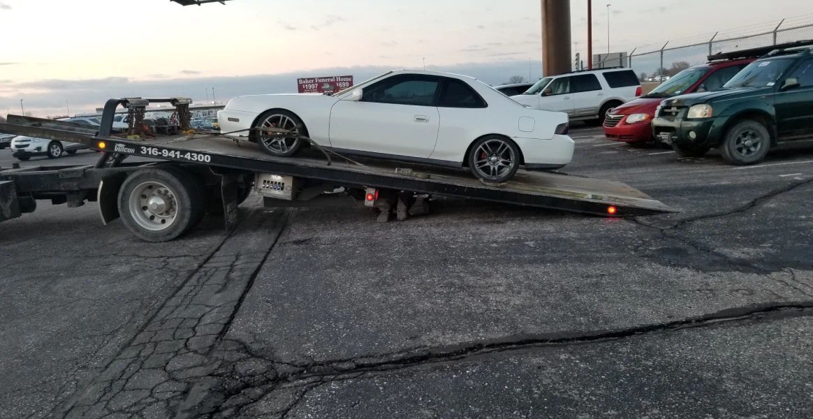 A white car is sitting on top of a tow truck.