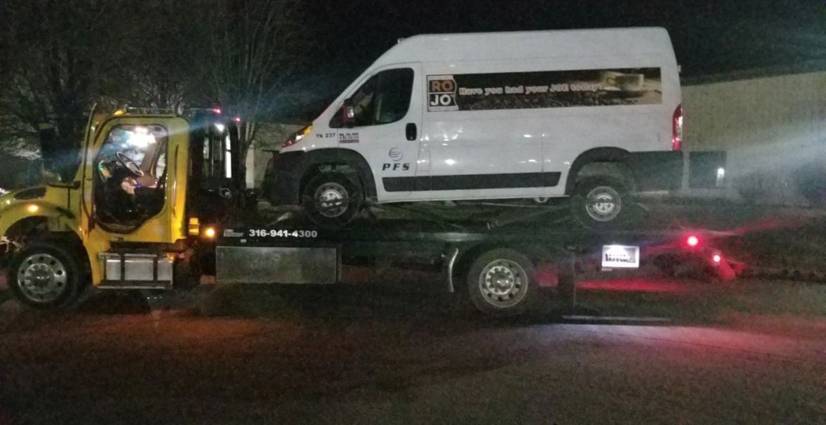 A white van is being towed by a yellow tow truck.