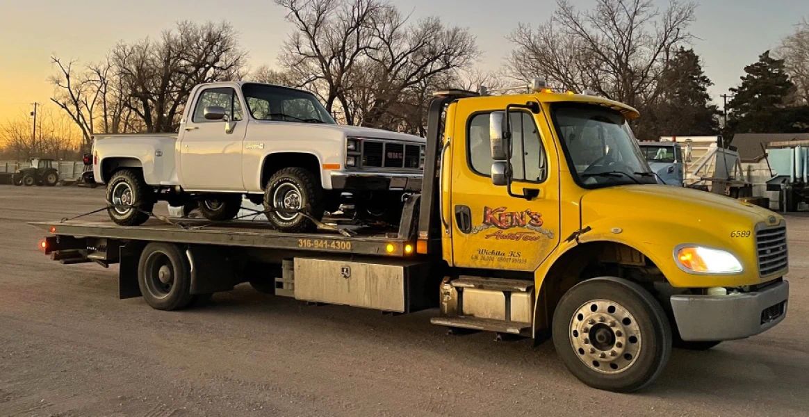 A yellow tow truck is towing a white truck.