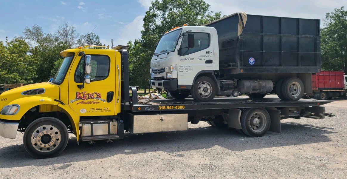A yellow tow truck is towing a dump truck.