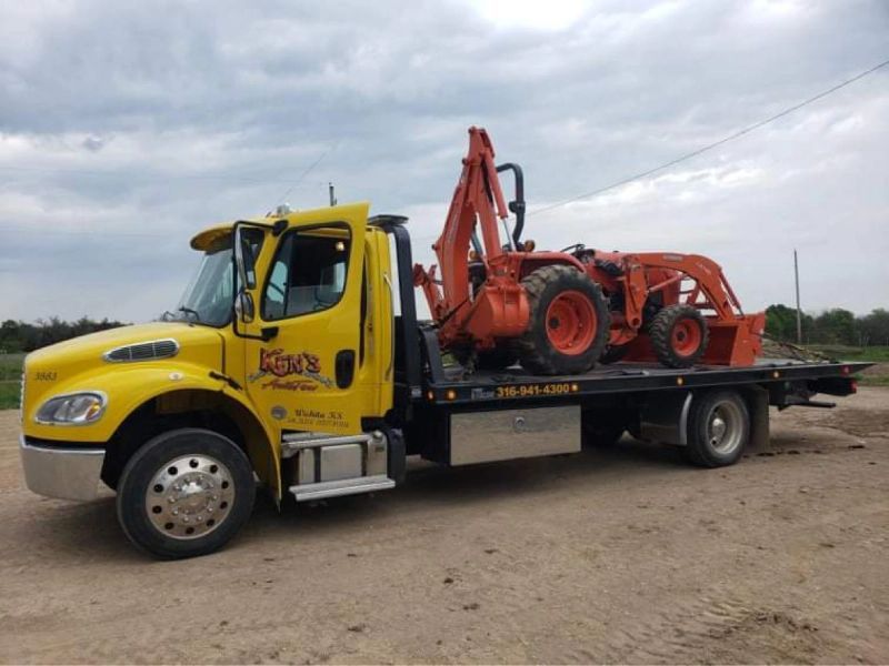 A yellow tow truck is carrying an orange tractor