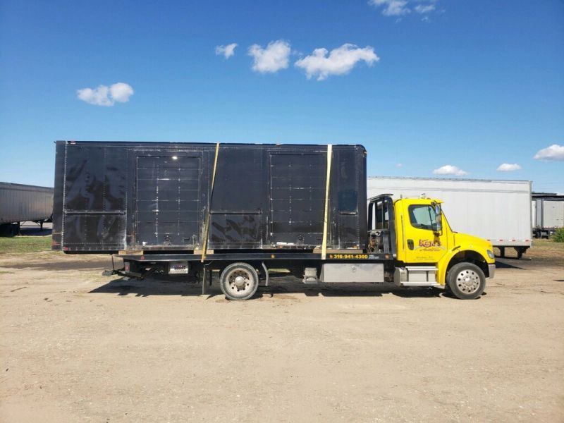 A yellow tow truck is carrying a large black box.
