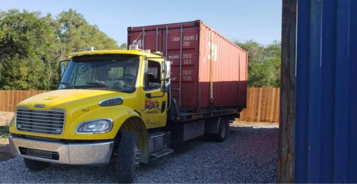 A yellow truck is carrying a red shipping container.