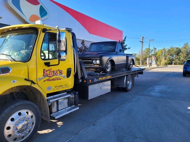 A yellow tow truck is towing a black truck.