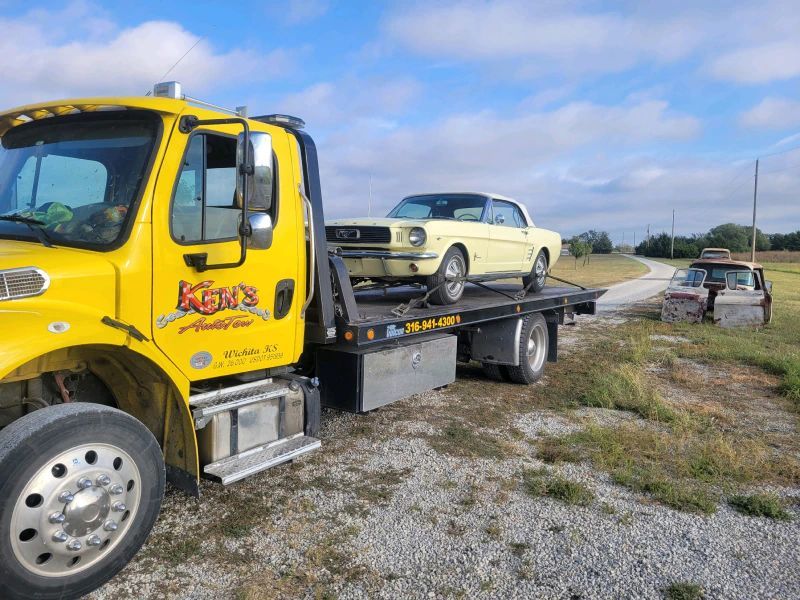 A yellow tow truck is carrying a mustang on the back of it.