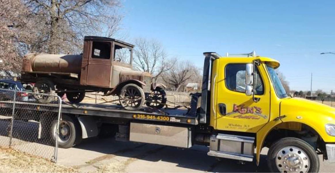 An old truck is being towed by a yellow tow truck.