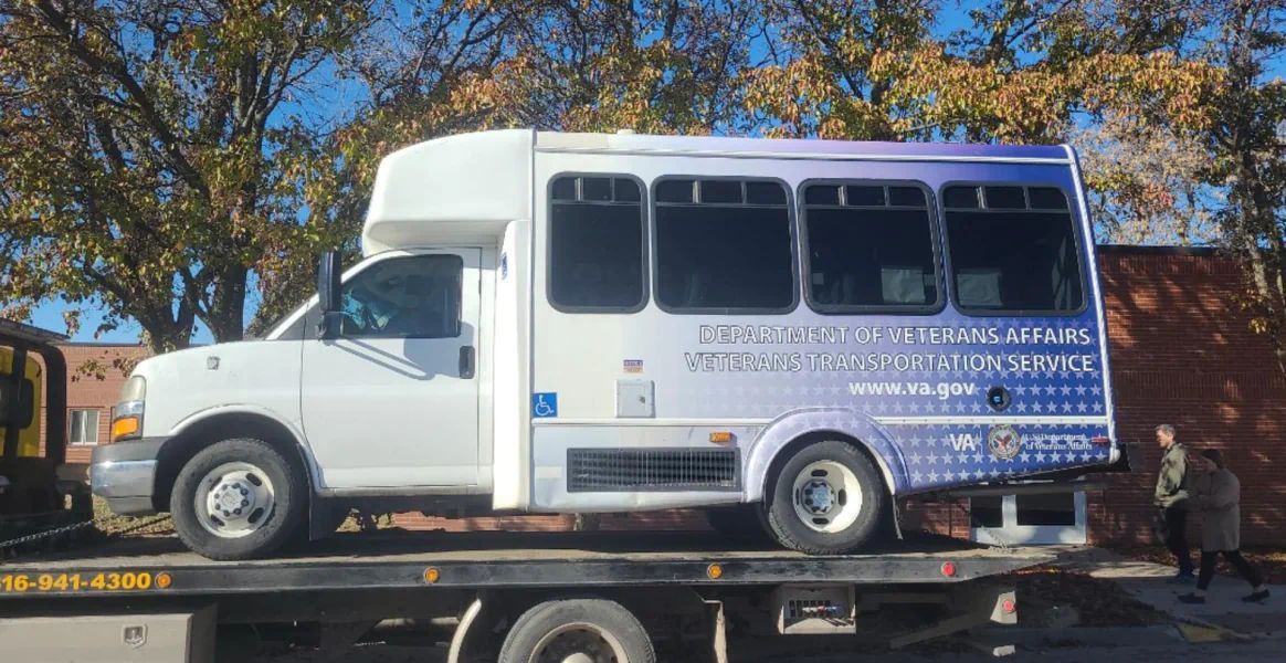 A white and purple bus is sitting on top of a tow truck.