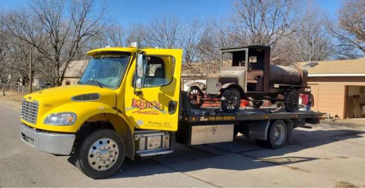 A yellow tow truck is carrying a car on the back of it.