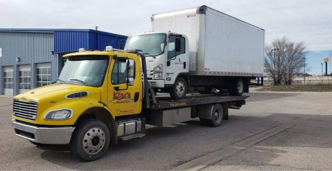 A yellow tow truck is towing a white truck in a parking lot.