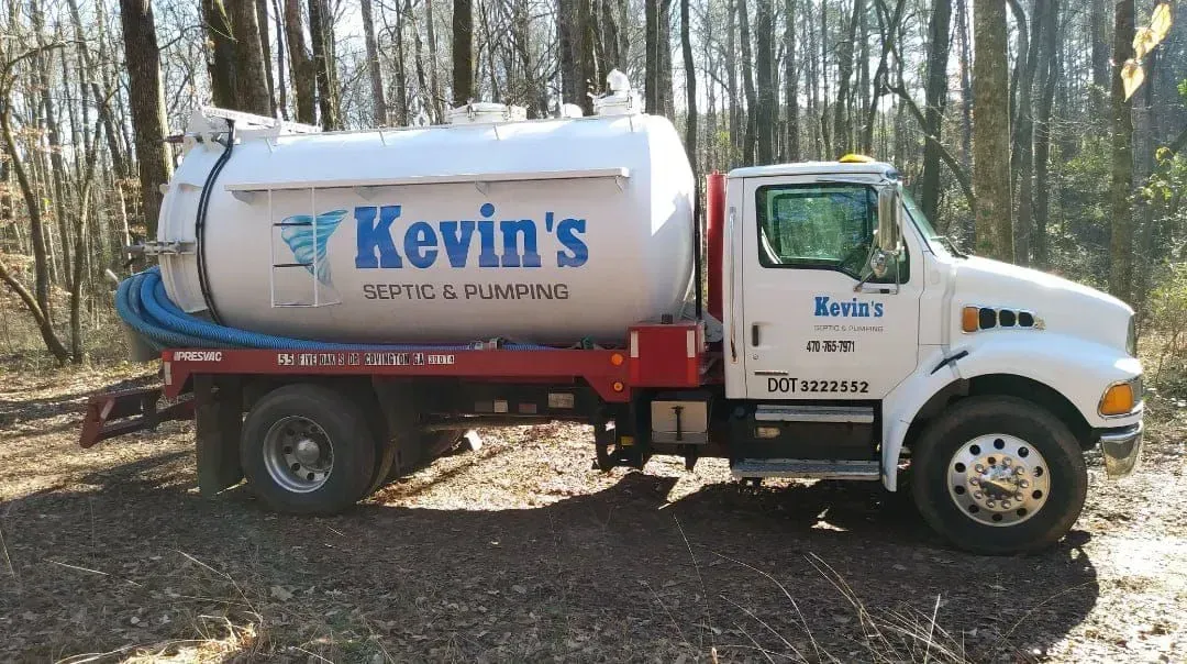 White septic tank truck with Kevin's logo parked outdoors, possibly wooded area.