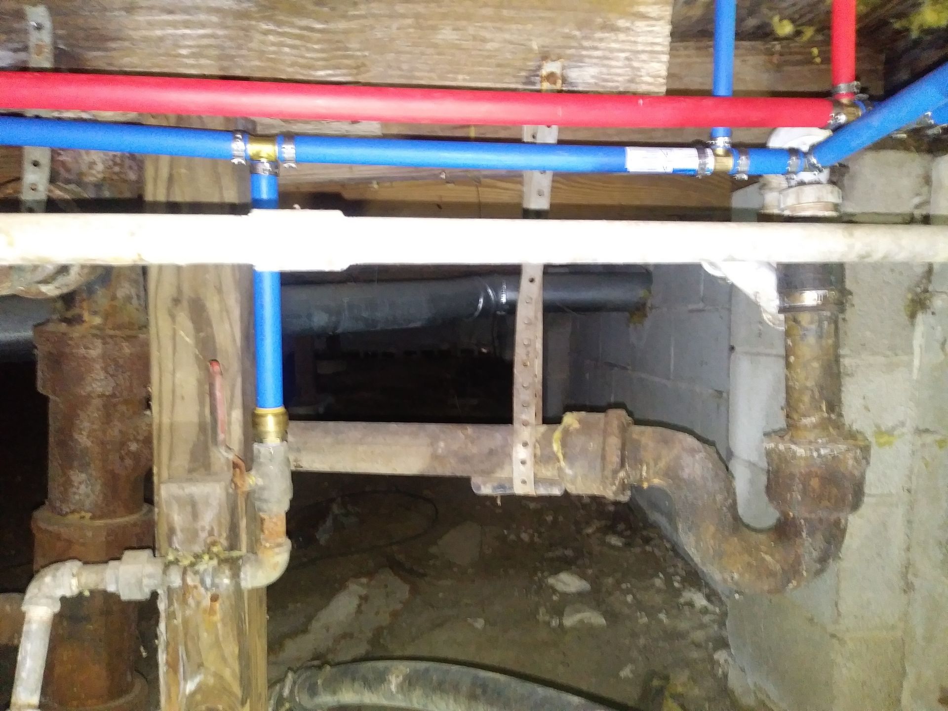 Plumbing pipes in a basement. Blue and red plastic pipes with copper connections are attached to older, rusty metal pipes.