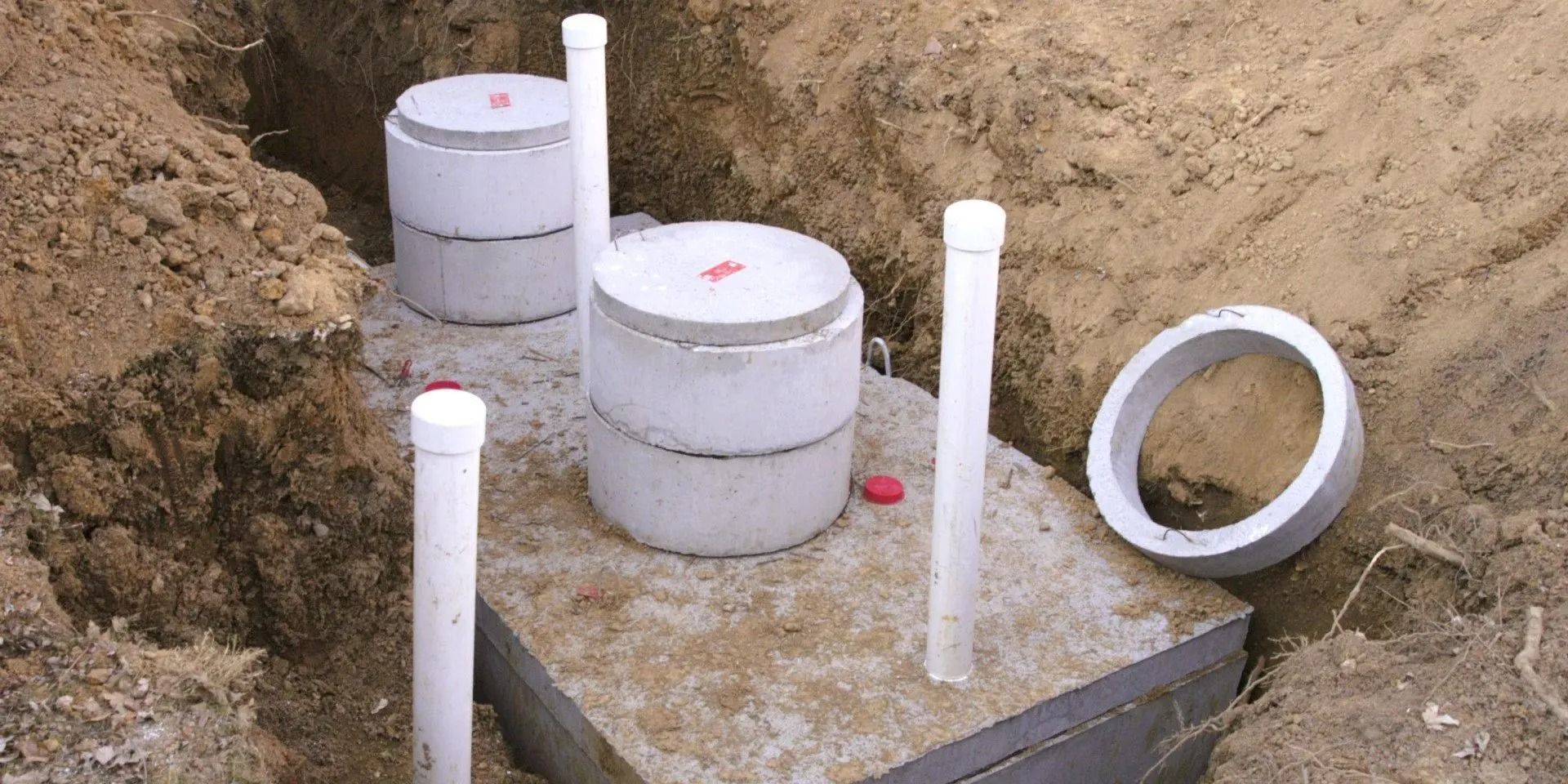 Construction site with concrete septic tanks and white pipes in trenches of dirt.