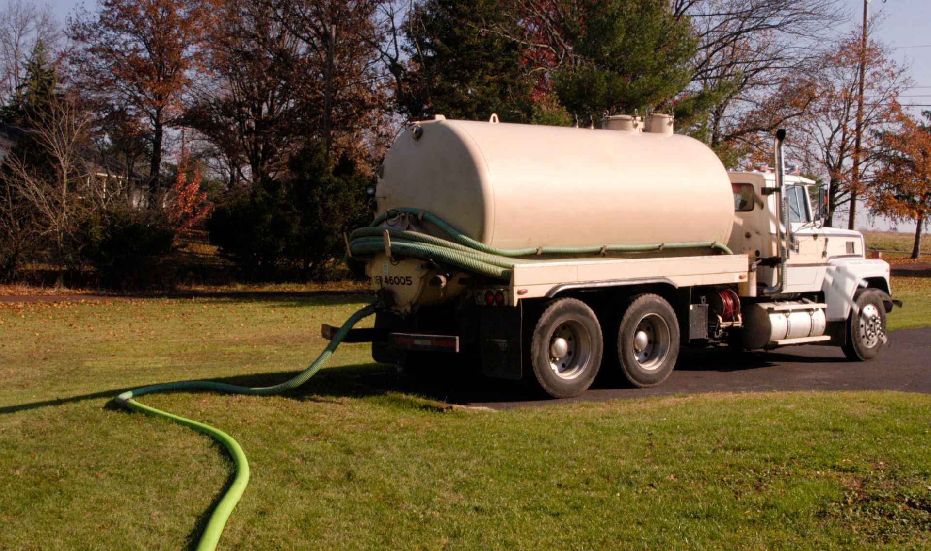 Septic tank truck on a grassy lawn with a green hose extended.