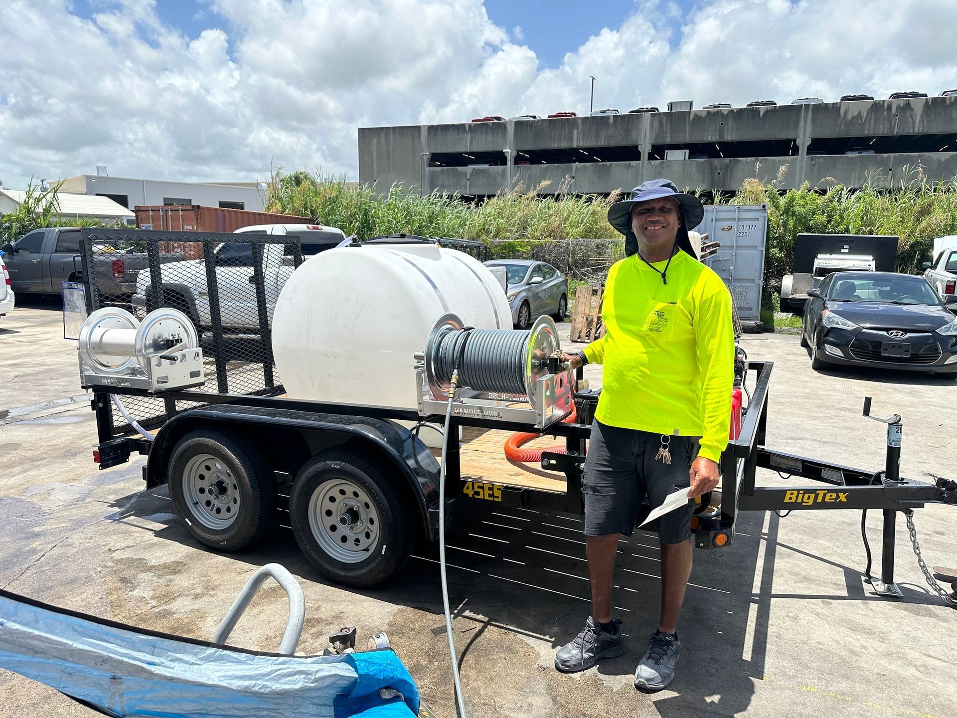 Person standing beside a white trailer in a parking lot, wearing a neon yellow shirt and black shorts