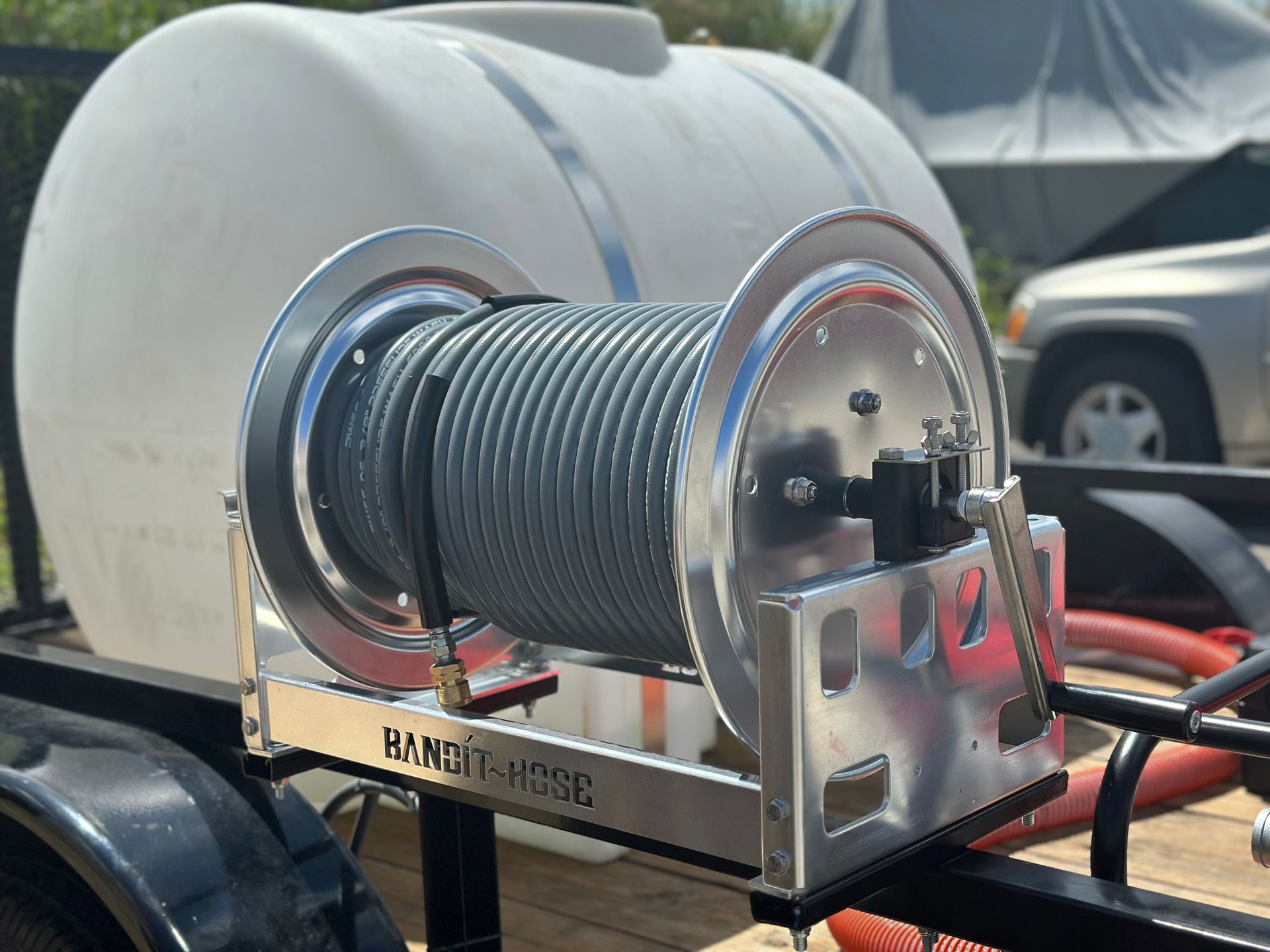 Industrial hose reel mounted on a trailer, with coiled black hose and metal housing outdoors.