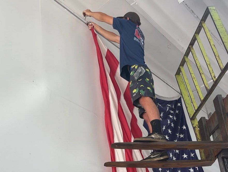 Person hanging a large American flag on an indoor staircase, reaching up near the ceiling.