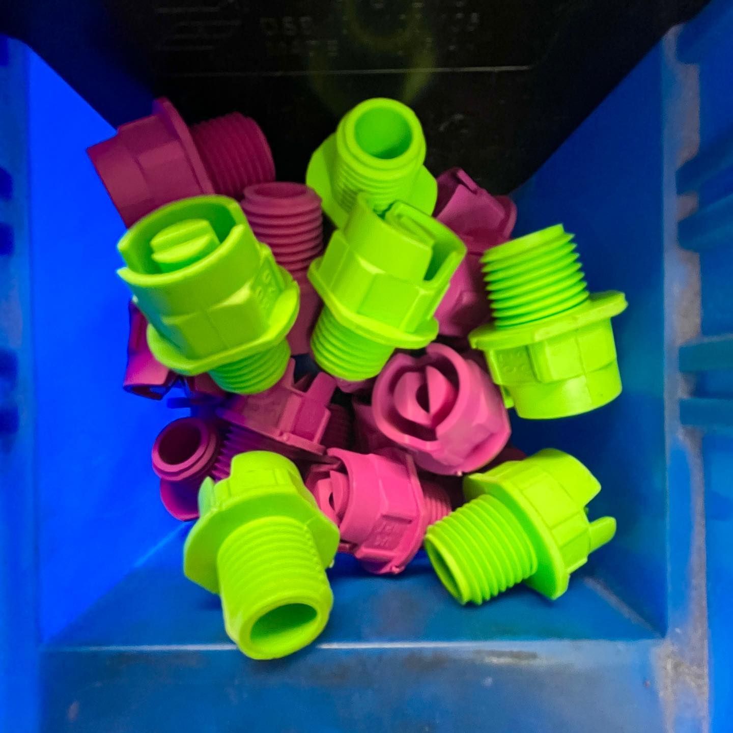 Neon green and pink plastic threaded fittings piled in a blue bin